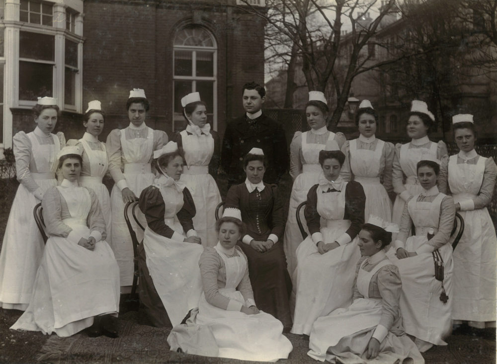 A large group of hospital staff in uniforms posing in the grounds of the hospital, c. 1900