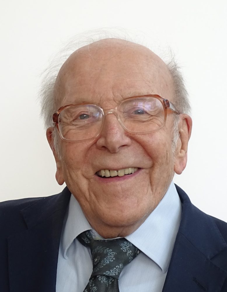 Photo of Douglas Chamberlain wearing brown rimmed glasses, shirt, tie and dark blazer.