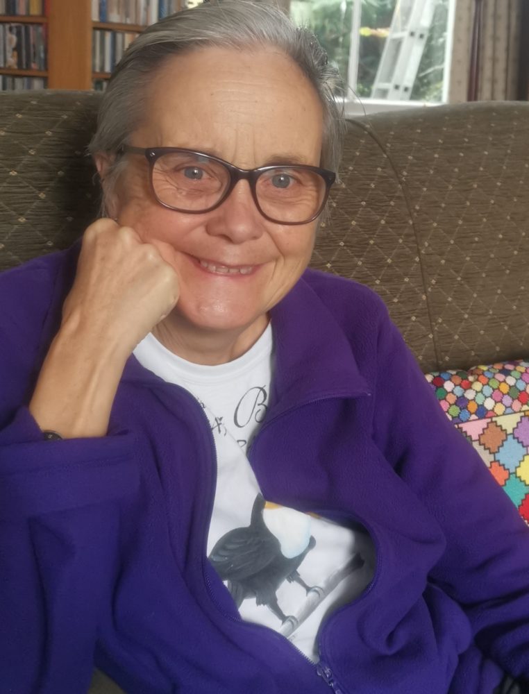 Photo of Ashley Adsett wearing a purple cardigan. Ashley is smiling looking towards the camera.