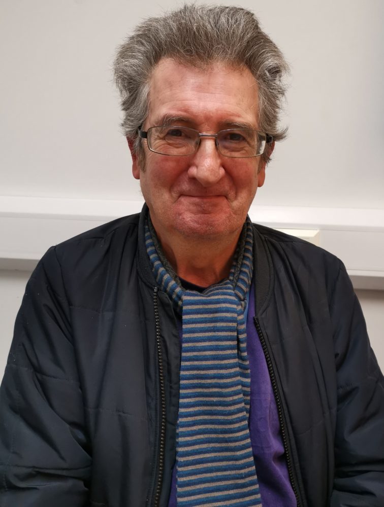 Photo of Gary Scarfield with a little happy grin, wearing black jacket and striped t-shirt.