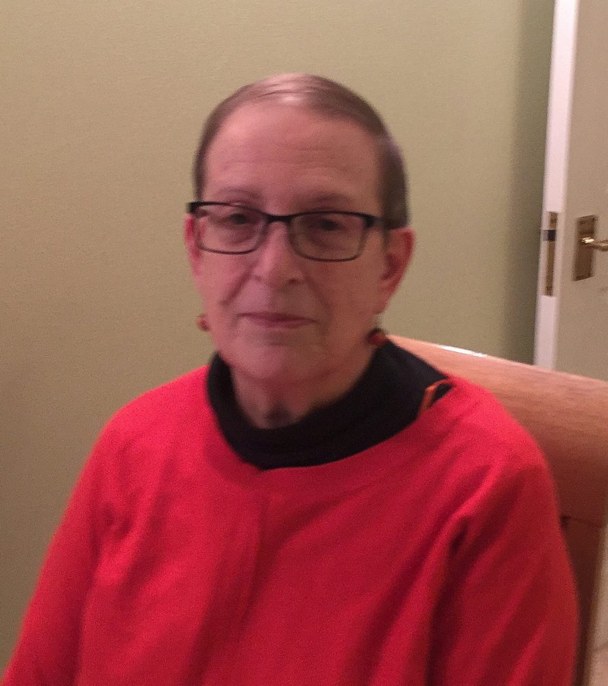 Photo of Helen Brownstone wearing a bright red jumper and glasses.